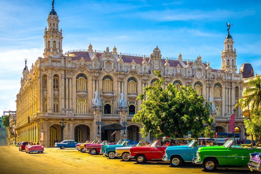 Autos clásicos estacionados frente al ornamentado Gran Teatro de La Habana, Cuba, bajo un cielo azul brillante.