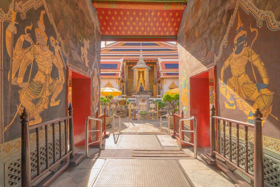 Entrada a un templo de color dorado con murales en las paredes; detalles ornamentados y una estatua visible en la distancia.