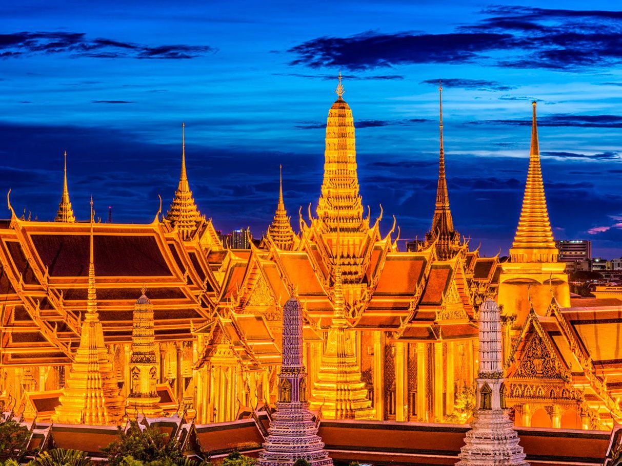 Edificios de torres doradas del Gran Palacio de Bangkok, Tailandia, iluminados al anochecer con un cielo azul.