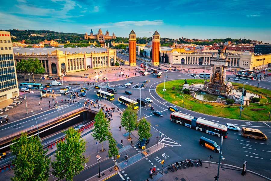 Vista aérea de la Plaza de España en Barcelona con tráfico, edificios y dos altas torres venecianas.