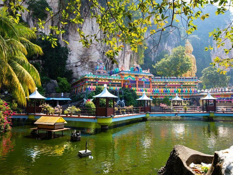 Un complejo de templos hindúes coloridos reflejado en un estanque, situado frente a un acantilado rocoso.