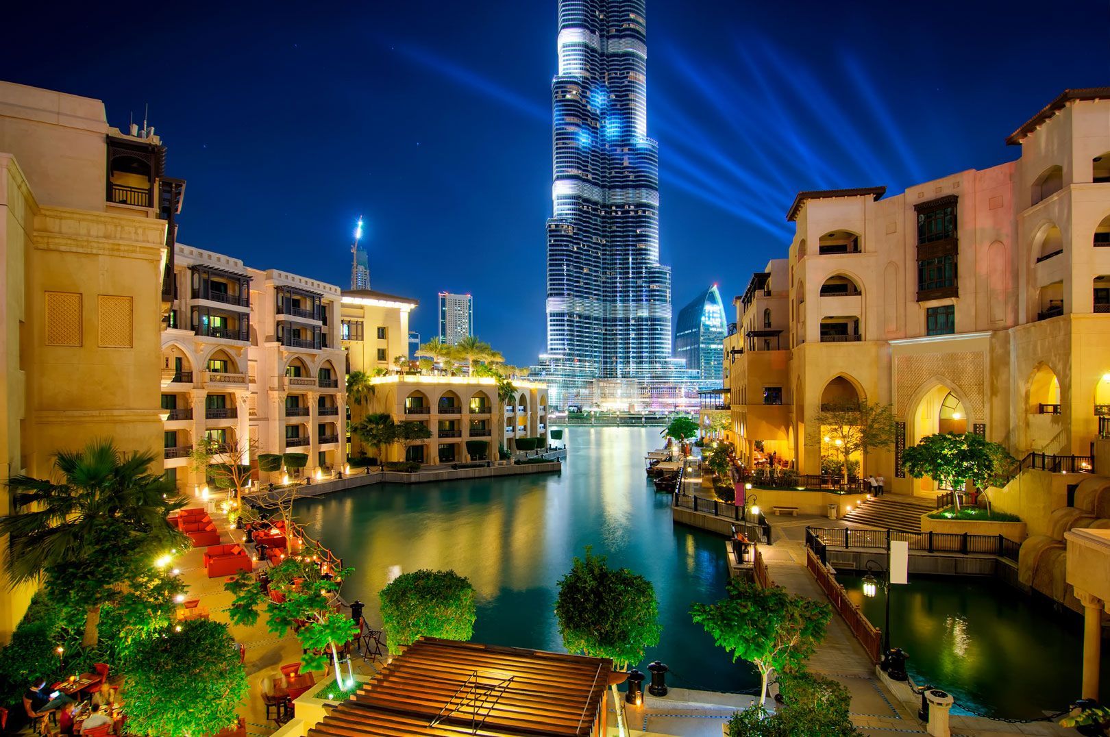Vista nocturna de Dubái, con el rascacielos Burj Khalifa elevándose sobre edificios y un canal. Las luces iluminan la escena.