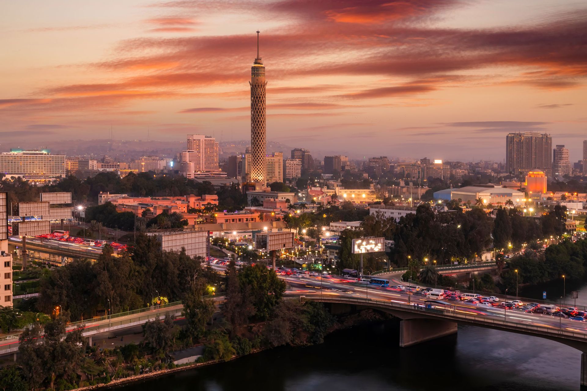 Horizonte de El Cairo al atardecer, con la Torre de El Cairo en el centro. Un puente con tráfico cruza un río.