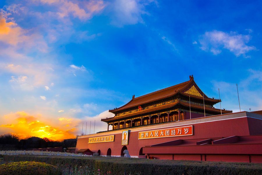 Puerta de Tiananmen en Pekín al atardecer con un cielo colorido; una gran estructura roja con detalles dorados ornamentados.