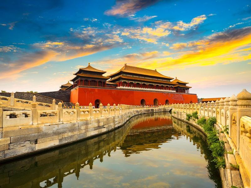 La Ciudad Prohibida en Beijing, China, con paredes rojas, tejados dorados y un foso reflectante contra el cielo del atardecer.