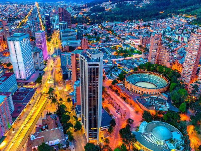 Vista aérea de Bogotá, Colombia, al anochecer con luces de la ciudad iluminando edificios y calles, incluida una gran plaza de toros.