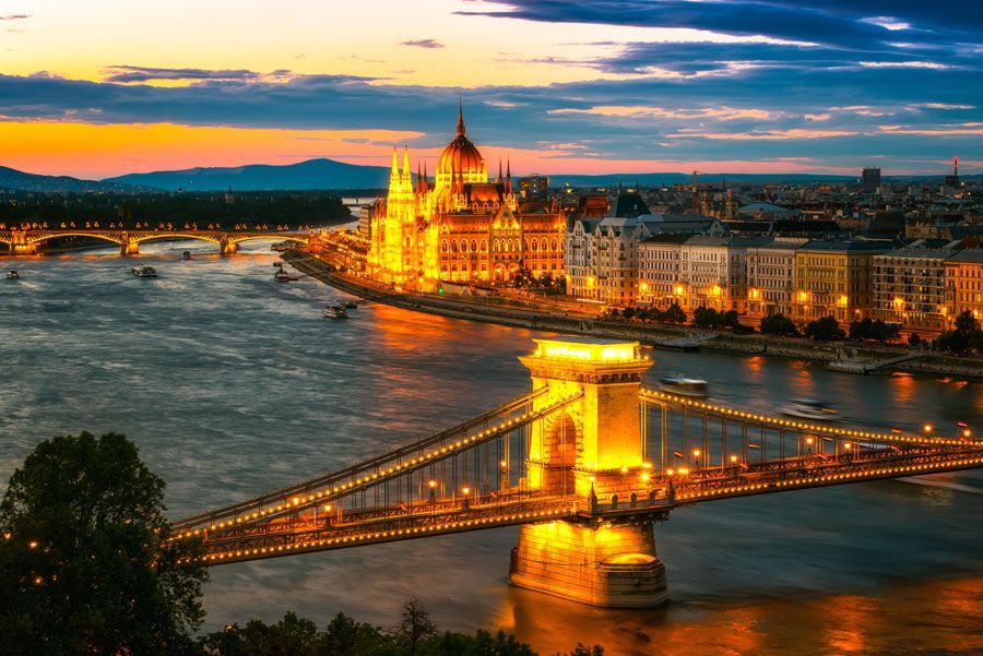Una vista nocturna de Budapest, Hungría, con el edificio del Parlamento iluminado, el Puente de las Cadenas y el río Danubio al atardecer.