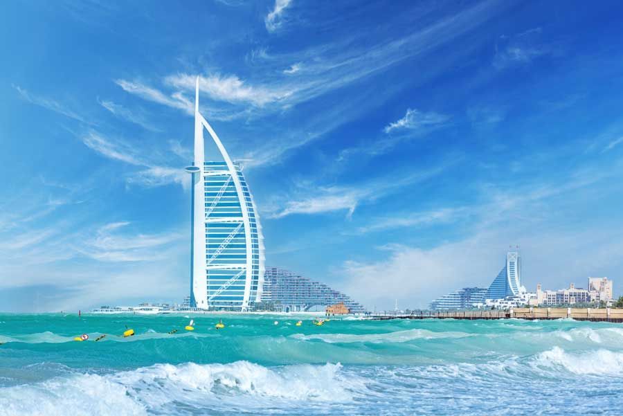 Hotel Burj Al Arab en Dubai, un edificio con forma de vela en la costa con agua turquesa y un cielo azul.
