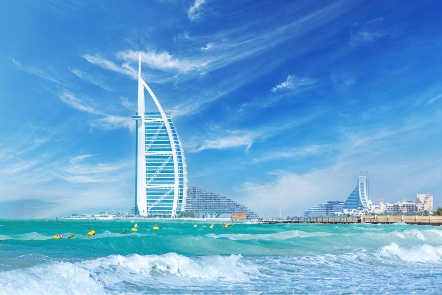 El hotel Burj Al Arab de Dubai, una estructura blanca con forma de vela, se eleva sobre aguas turquesas bajo un cielo azul brillante.