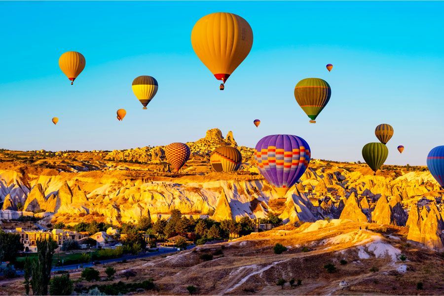 Globos aerostáticos de varios colores flotan sobre un paisaje erosionado e iluminado por el sol en Capadocia, Turquía.