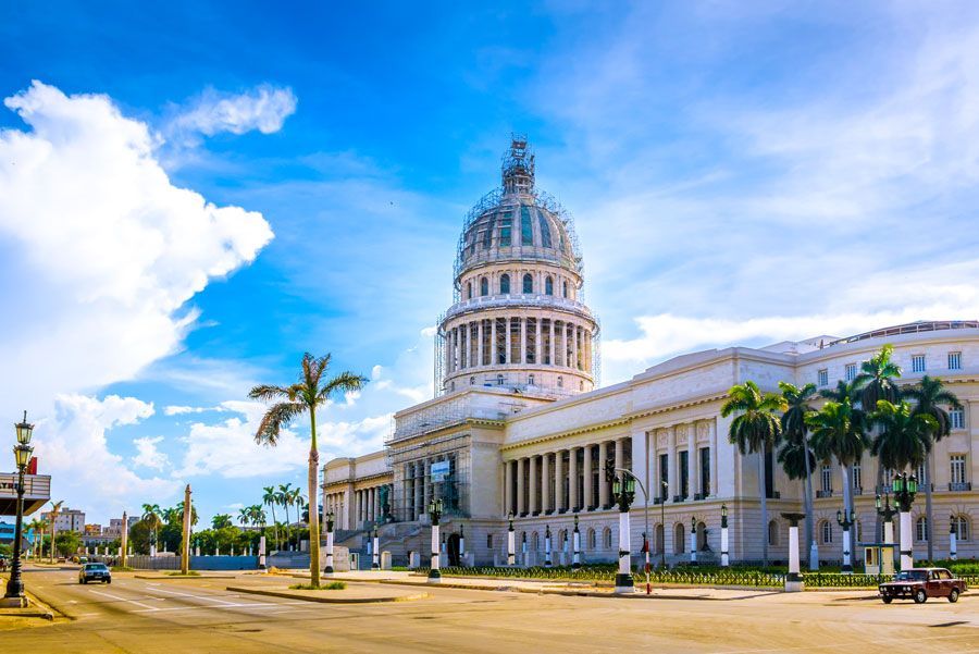 Edificio del Capitolio en La Habana, Cuba, un gran edificio blanco con una cúpula prominente, bajo un cielo azul brillante con palmeras que bordean la calle.