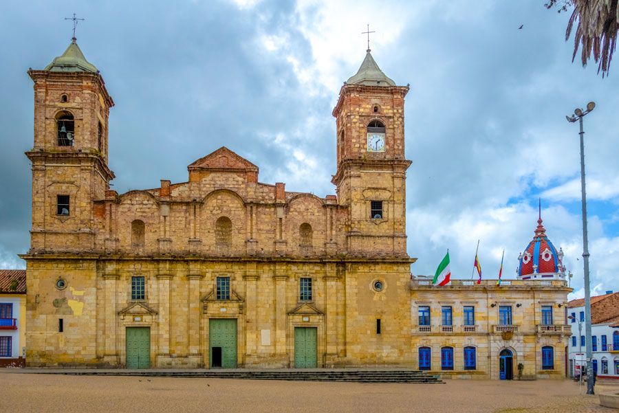 Iglesia y edificio gubernamental en una plaza de la ciudad, con dos torres de ladrillo y una fachada de color crema, bajo un cielo nublado.