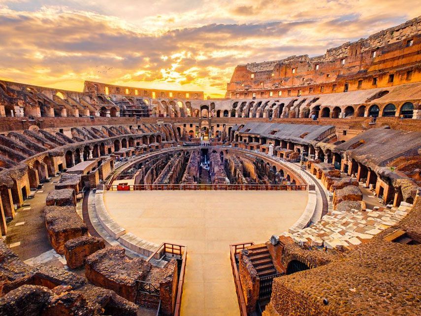 El interior del Coliseo al atardecer. La piedra beige de las ruinas contrasta con el cielo dorado.
