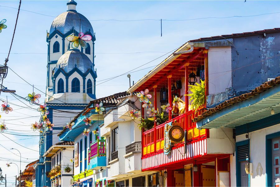 Colorida escena callejera en Salento, Colombia, con una torre de iglesia y casas con balcones.