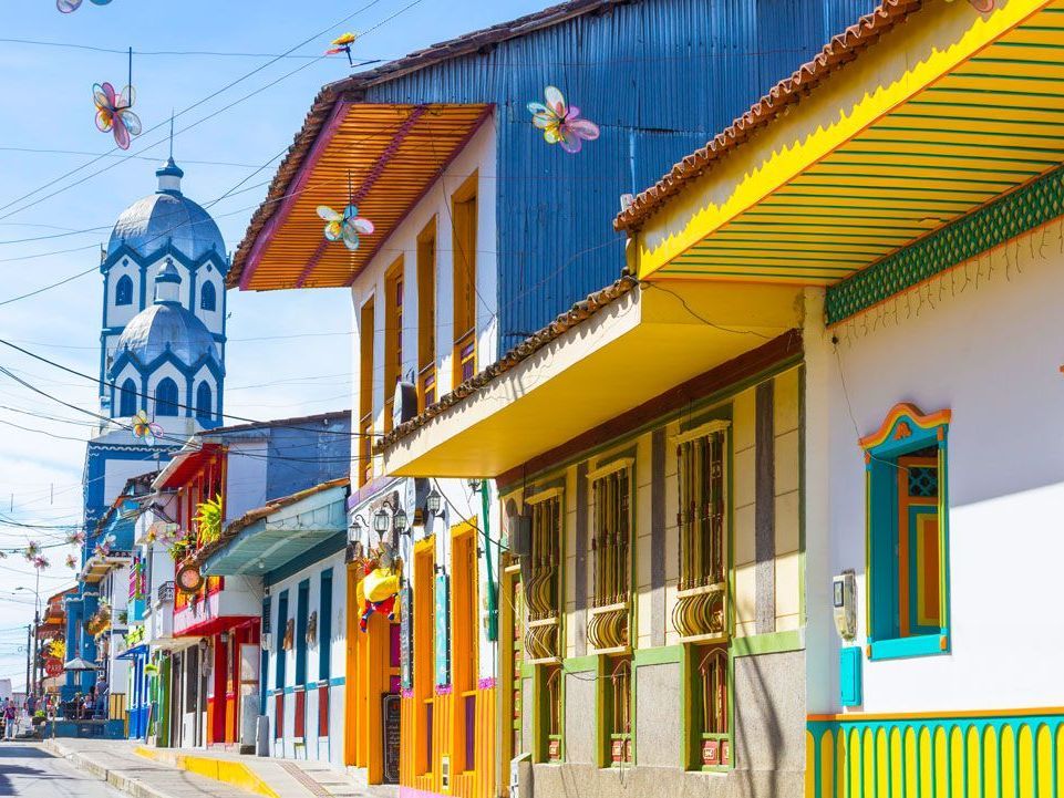 Colorida escena callejera en Guatapé, Colombia, con edificios vibrantes y una torre de iglesia al fondo.