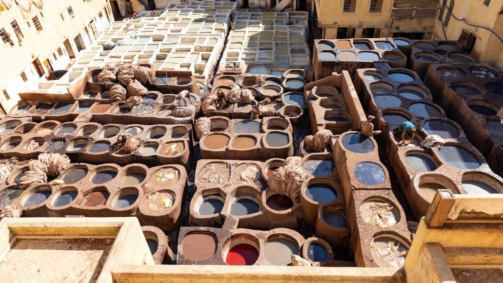 Curtidurías en Fez, Marruecos. Los trabajadores se encuentran entre numerosas tinas de piedra con tintes; la escena está llena de vibrantes colores y texturas.