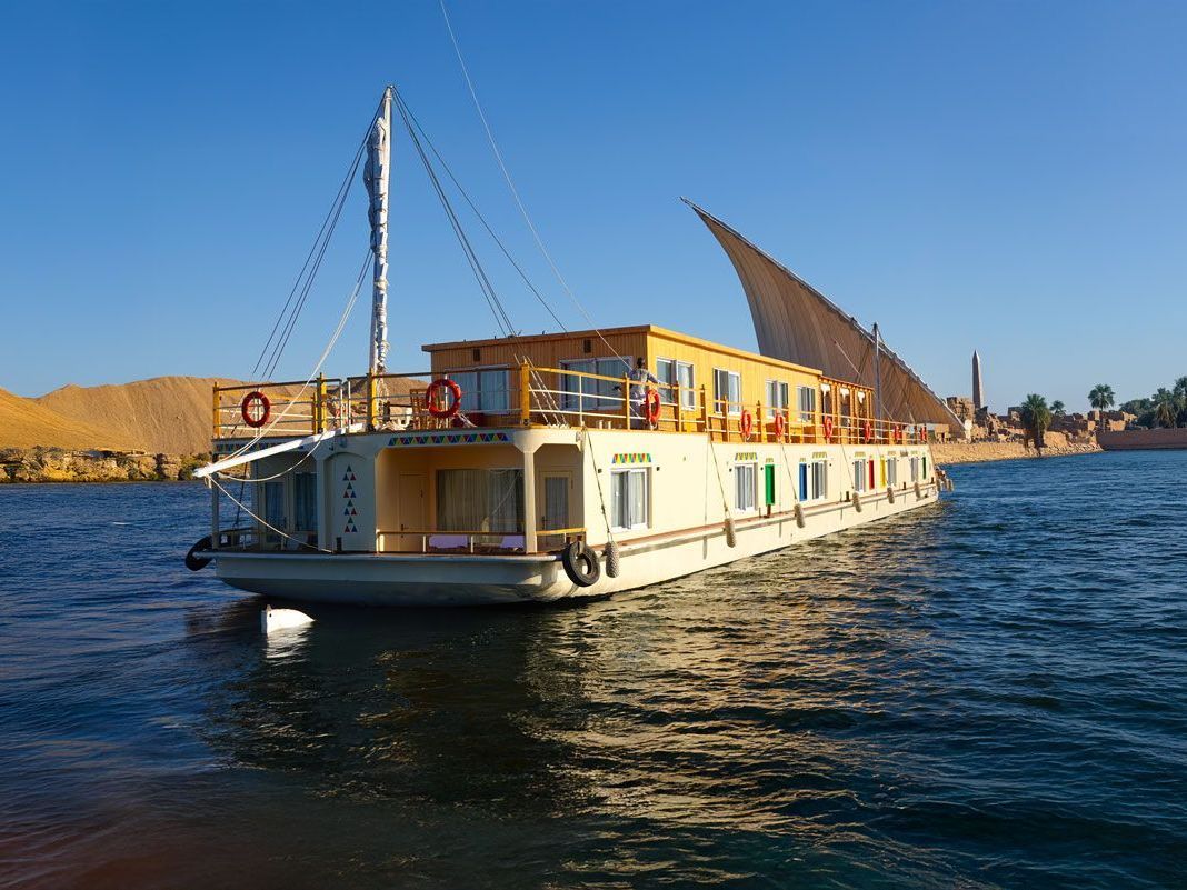 Casa flotante navegando en un río en Egipto con un exterior de color amarillo claro y un cielo azul claro.