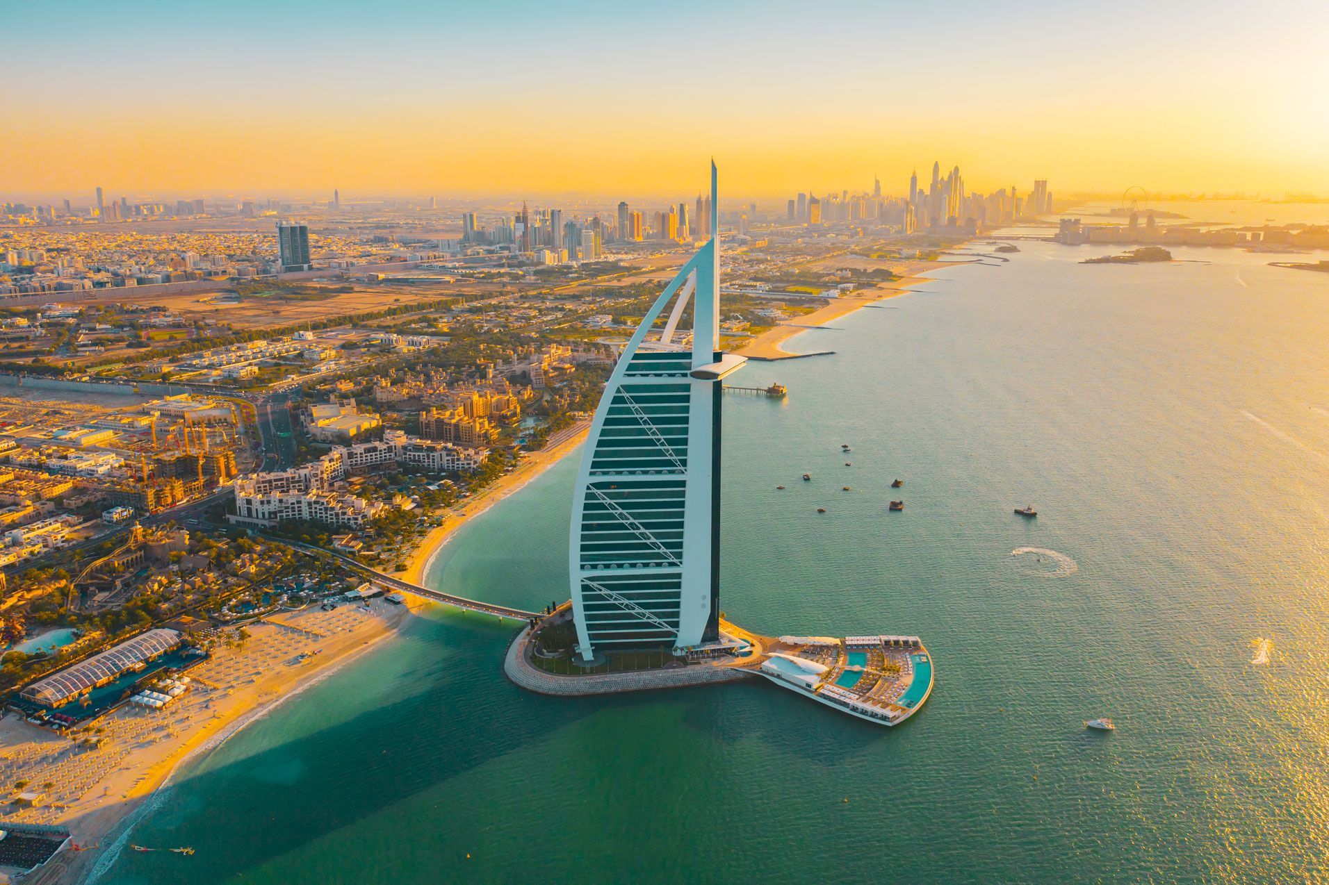 Hotel Burj Al Arab en una isla artificial en Dubai, bañado por la cálida luz del atardecer, con vistas al horizonte de la ciudad y a la playa.