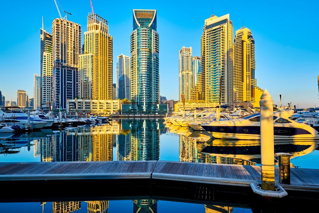 El horizonte de Dubai Marina con rascacielos y yates en un puerto, reflejándose en el agua en un día soleado.