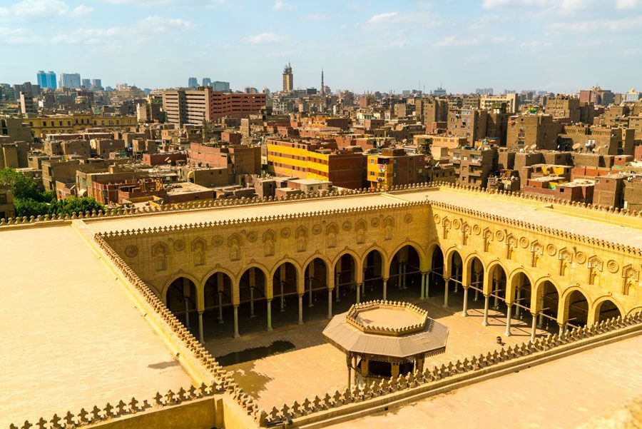 Vista aérea de El Cairo, Egipto, con un gran patio en primer plano, rodeado de columnatas arqueadas y un denso paisaje urbano.