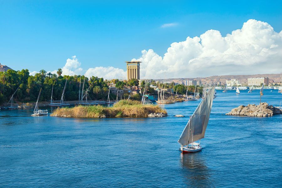 Veleros en el río Nilo, cerca de la ciudad de Asuán, Egipto, con una torre y cielo azul.