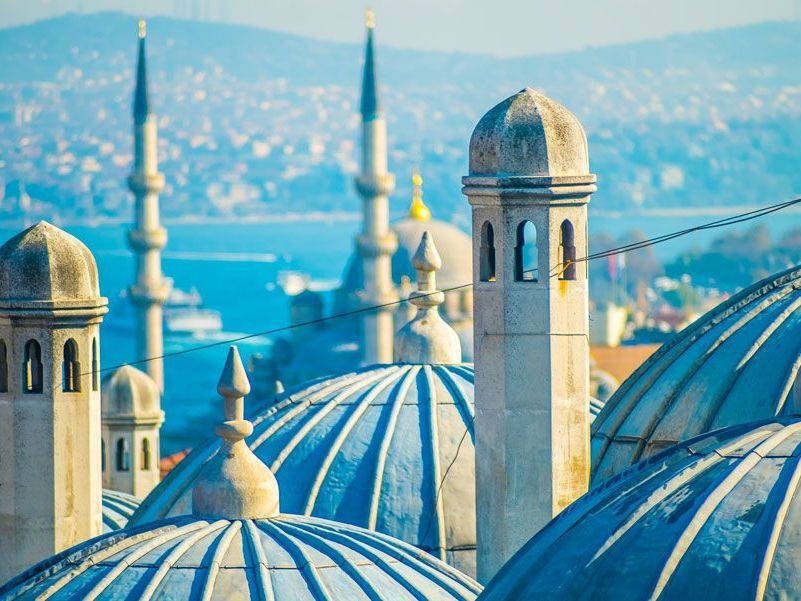 Cúpulas azules y minaretes de una mezquita en Estambul, Turquía, con un mar azul y un paisaje urbano de fondo.