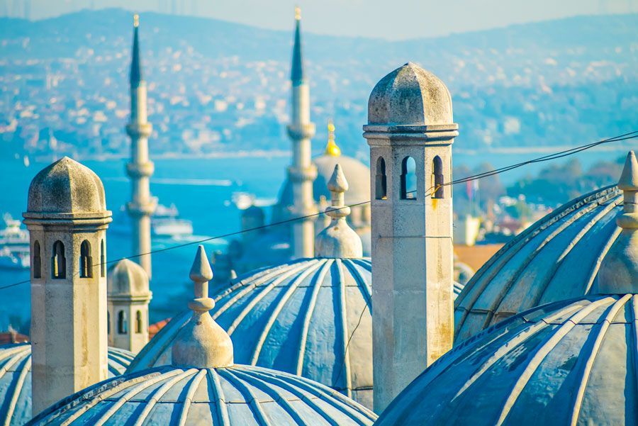 Mezquita de cúpula azul con minaretes contra un cielo azul brillante, con vista al paisaje urbano y al agua.