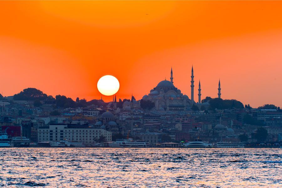 Puesta de sol sobre Estambul, Turquía, con la silueta de una mezquita y minaretes contra el cielo naranja.