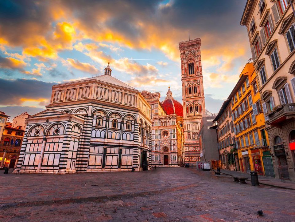 Florencia, Italia: Catedral de Santa María del Fiore, Baptisterio y Campanile de Giotto contra un cielo al atardecer, en una plaza pavimentada.