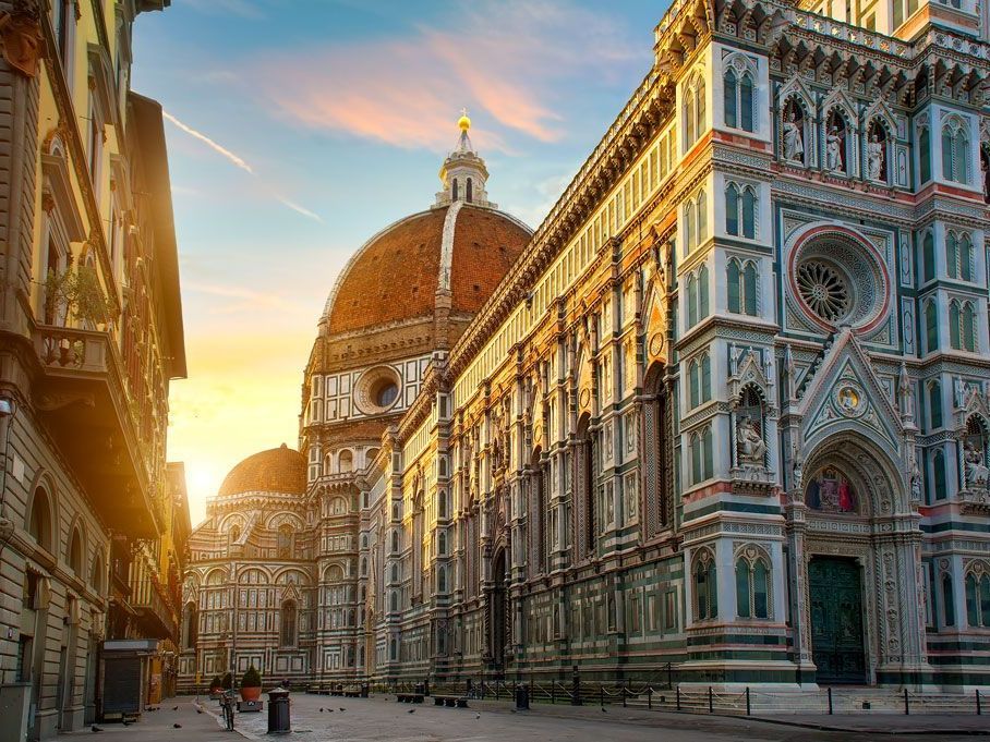 Exterior de la Catedral de Florencia al atardecer, con fachada ornamentada, gran cúpula y edificios que bordean la calle.