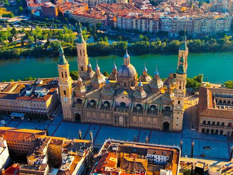 Vista aérea de la Basílica de Nuestra Señora del Pilar en Zaragoza, España, con el río verde y los edificios de la ciudad.