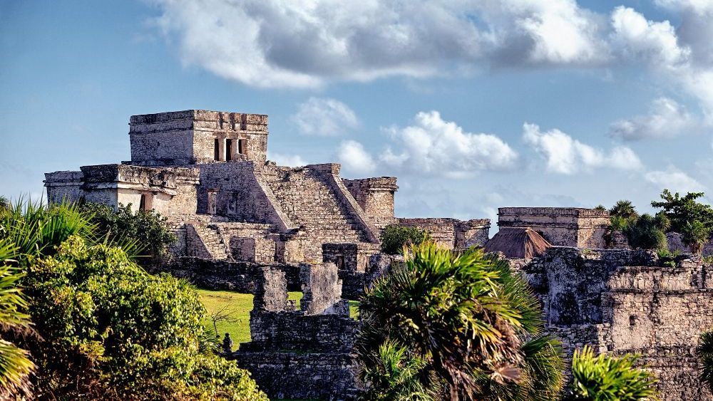 Antiguas ruinas mayas en un acantilado con vistas al mar Caribe, bajo un cielo azul con nubes hinchadas.