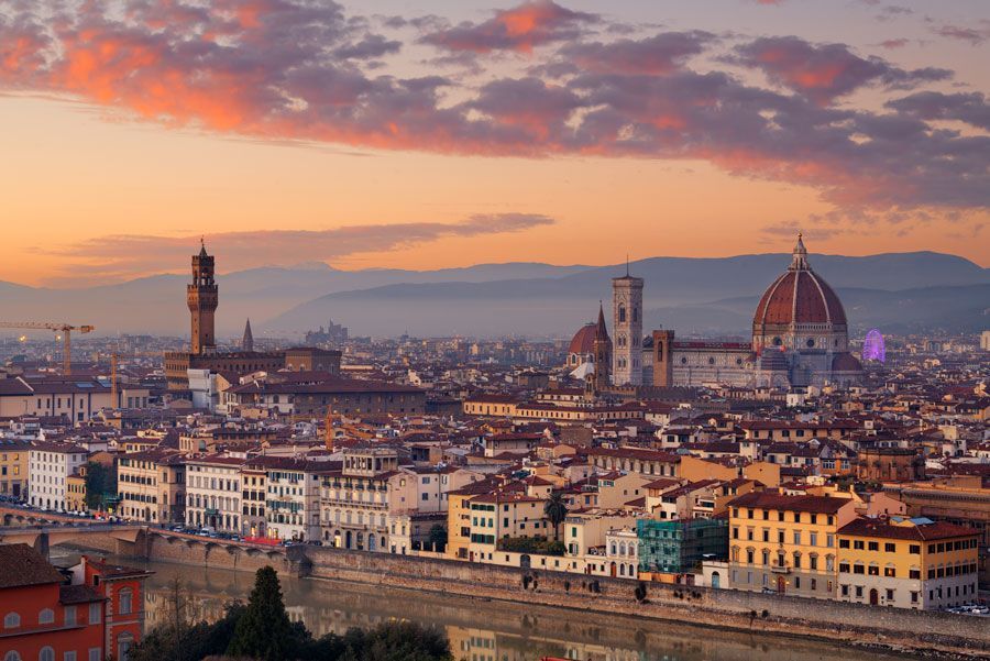 Paisaje urbano de Florencia, Italia, al atardecer. Los edificios bordean el río Arno, con el Duomo y el Campanile de Giotto destacando sobre un cielo colorido.