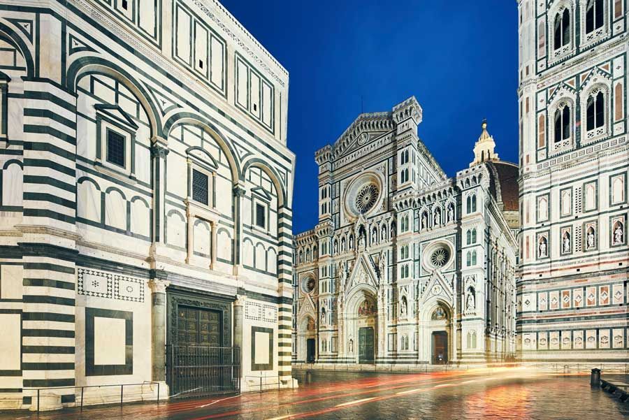 Catedral y Baptisterio de Florencia, Italia, de noche, con fachadas de mármol blanco y verde bajo un cielo azul oscuro.