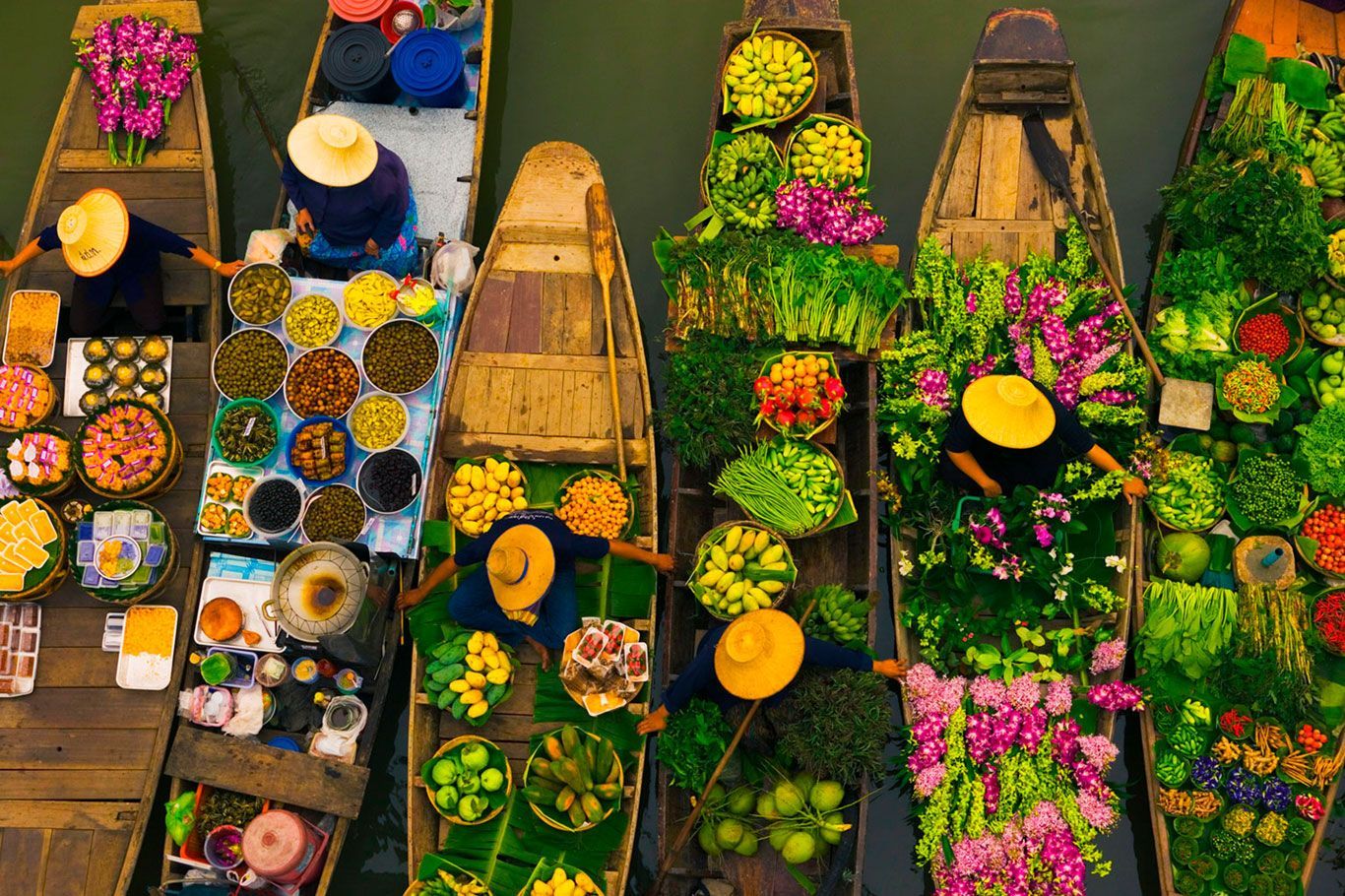 Barcos llenos de productos coloridos y flores en un mercado flotante, con gente con sombreros cónicos organizando y vendiendo productos.
