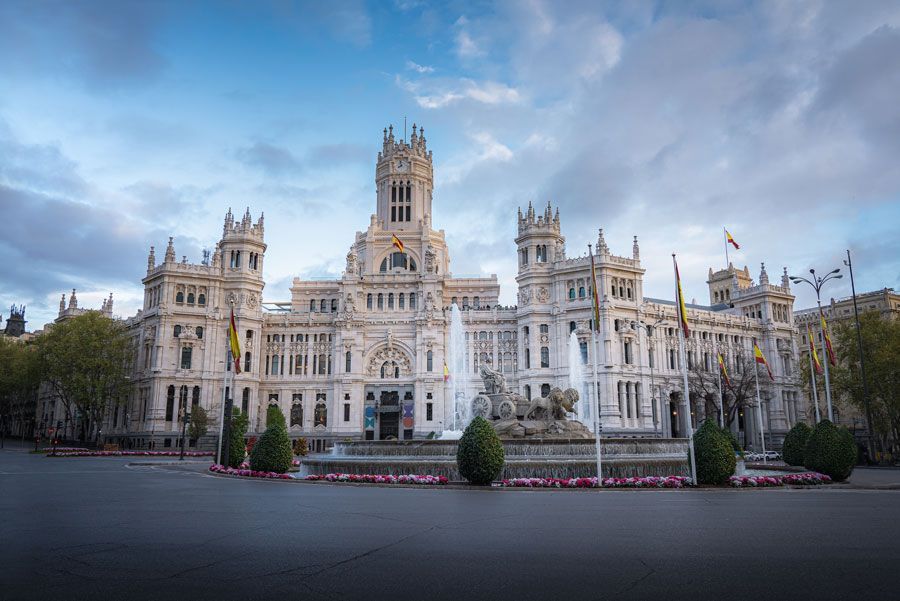 Palacio de Cibeles en Madrid, España, un gran edificio blanco adornado con una fuente en primer plano bajo un cielo azul.