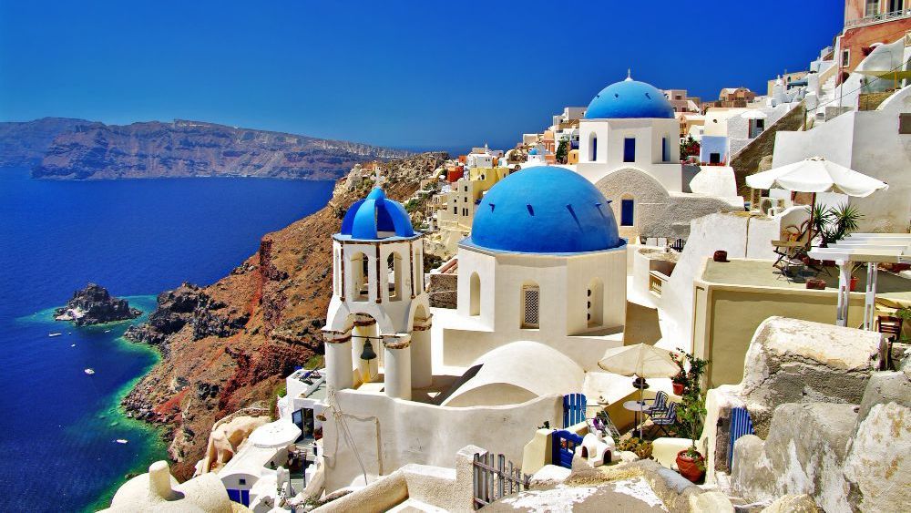 Edificios encalados con cúpulas azules en un acantilado con vistas al mar Egeo en Santorini, Grecia.