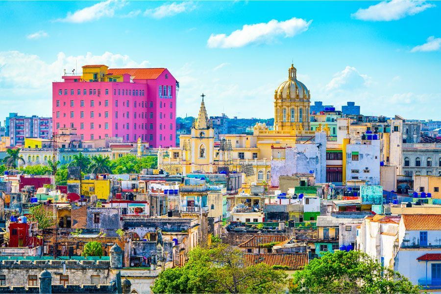 Colorido paisaje urbano de La Habana, Cuba, con edificios en tonos rosa, amarillo y azul bajo un cielo brillante.