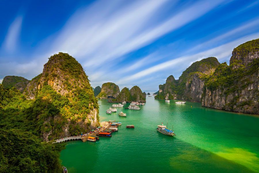 Aguas color esmeralda con barcos entre karsts de piedra caliza en la bahía de Ha Long, Vietnam, bajo un cielo azul brillante.