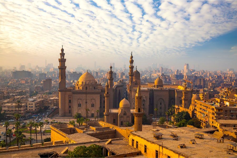 Paisaje urbano de El Cairo con una mezquita en primer plano, con minaretes y cúpulas contra un cielo nublado.