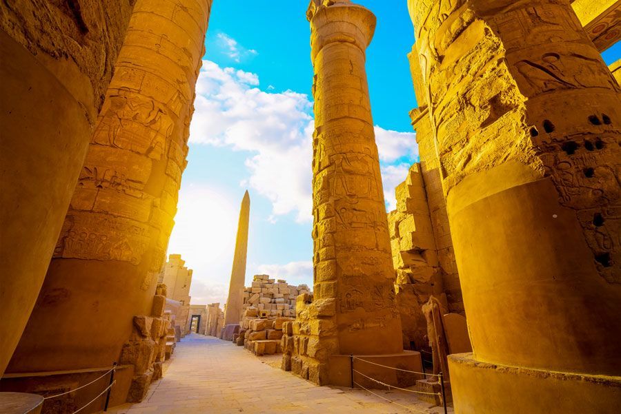 Columnas de piedra y un obelisco en el Templo de Karnak en Luxor, Egipto, con un cielo azul brillante y luz solar.