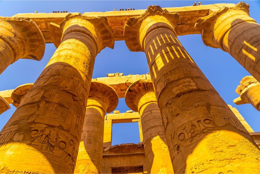Las antiguas columnas egipcias con jeroglíficos se alzan contra un cielo azul claro.