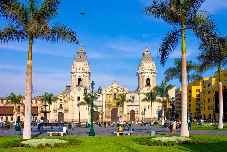 Catedral de Lima, Perú, con sus dos campanarios, en una plaza con palmeras y un cielo azul. Se ve gente en la plaza.