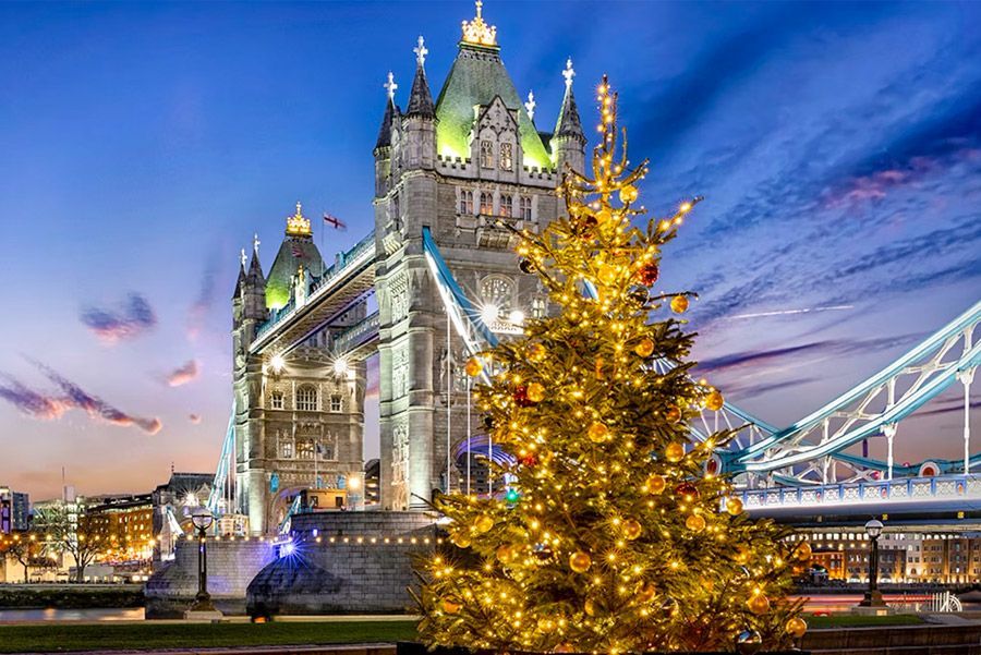 El Puente de la Torre de Londres al anochecer, con un árbol de Navidad decorado en primer plano. El puente está iluminado.