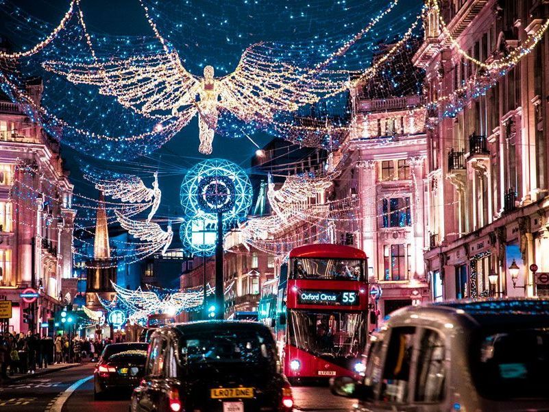 Regent Street en Londres de noche, decorada con luces navideñas, con un autobús rojo de dos pisos y coches en la carretera.