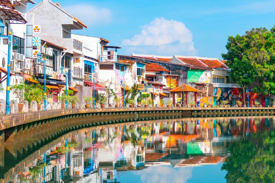 Hilera de edificios coloridos reflejados en un río tranquilo, bajo un cielo azul brillante.