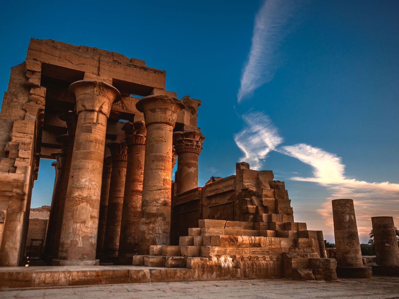 Ruinas de un antiguo templo egipcio con imponentes columnas, bañadas por una luz cálida contra un cielo azul profundo.