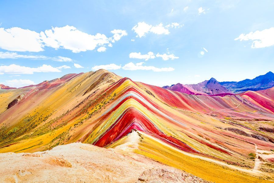 Montaña Arcoíris en Perú, con coloridas bandas de rocas rojas, amarillas y moradas bajo un cielo azul brillante.
