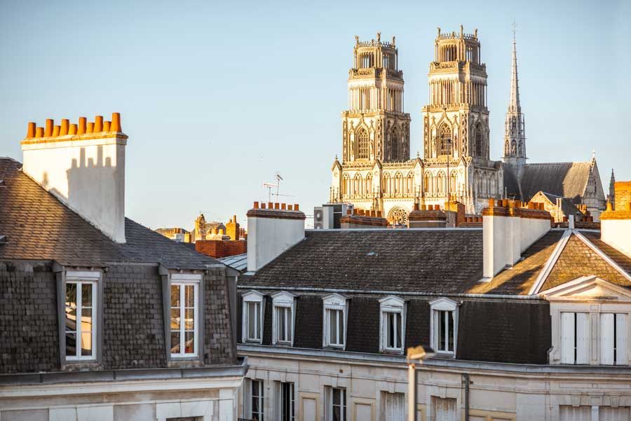 Tejados en primer plano con las torres de la Catedral de Orleans, Francia, elevándose al fondo bajo un cielo despejado.