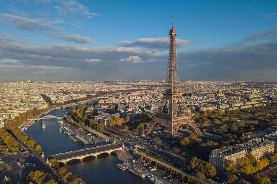 La Torre Eiffel en París, Francia, se alza sobre la ciudad y el río Sena bajo un cielo azul parcialmente nublado.